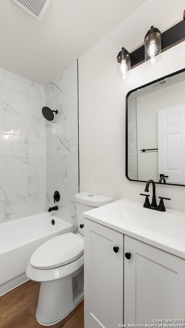 full bathroom with toilet, hardwood / wood-style floors, vanity, and tiled shower / bath combo