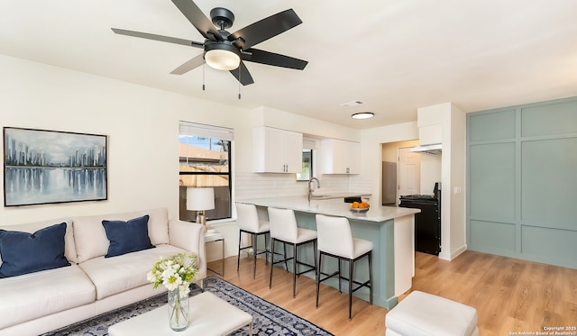 living room with light hardwood / wood-style floors, ceiling fan, and sink