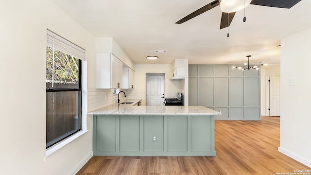 kitchen with stainless steel electric range, white cabinets, sink, light wood-type flooring, and kitchen peninsula