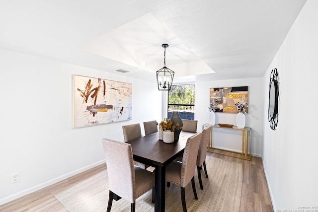 dining area featuring a tray ceiling, light hardwood / wood-style floors, and an inviting chandelier