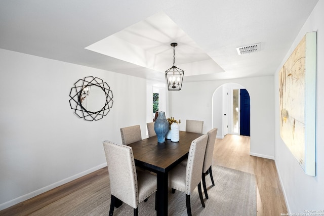 dining space featuring an inviting chandelier, light hardwood / wood-style flooring, and a raised ceiling