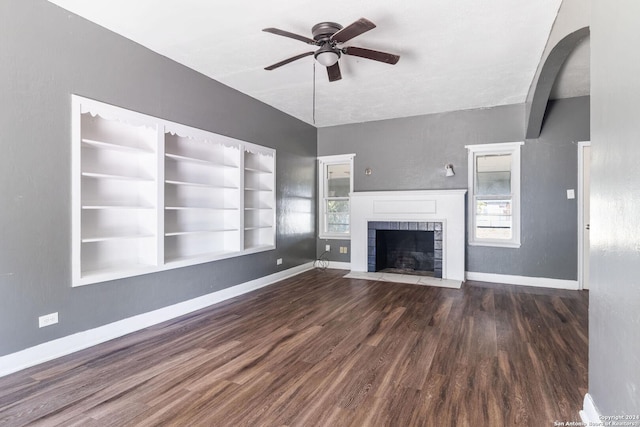 unfurnished living room with built in shelves, ceiling fan, a fireplace, and dark wood-type flooring