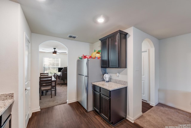 kitchen featuring light stone countertops, stainless steel fridge, dark brown cabinetry, ceiling fan, and dark hardwood / wood-style floors