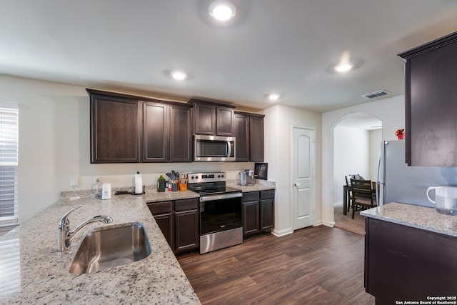 kitchen featuring appliances with stainless steel finishes, light stone counters, dark brown cabinetry, sink, and dark hardwood / wood-style floors