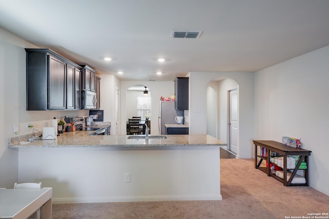 kitchen with light stone countertops, sink, kitchen peninsula, light carpet, and appliances with stainless steel finishes