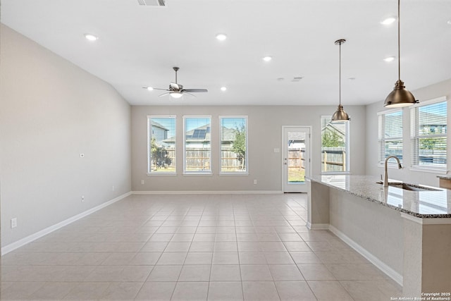 kitchen with light stone counters, ceiling fan, sink, pendant lighting, and plenty of natural light