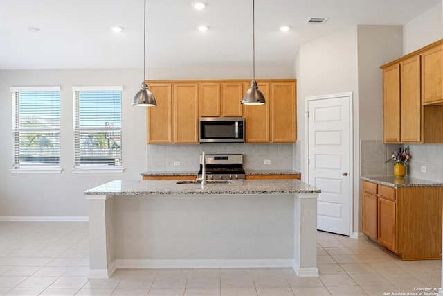 kitchen with a center island with sink, light stone countertops, hanging light fixtures, and appliances with stainless steel finishes