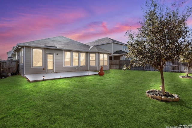 back house at dusk featuring a yard and a patio