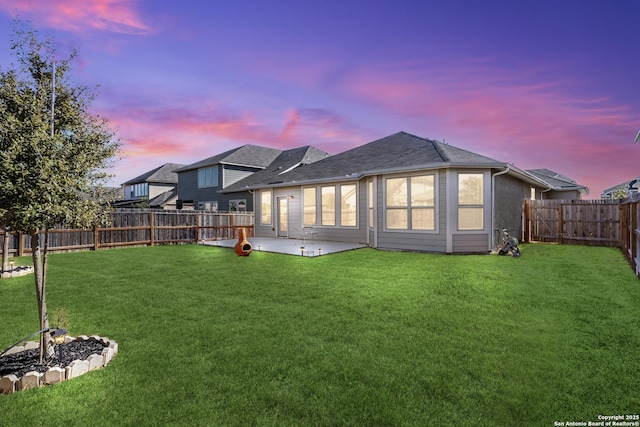 back house at dusk with a patio area and a yard