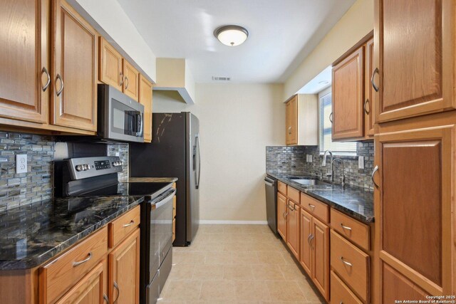 kitchen with backsplash, stainless steel appliances, dark stone counters, and sink