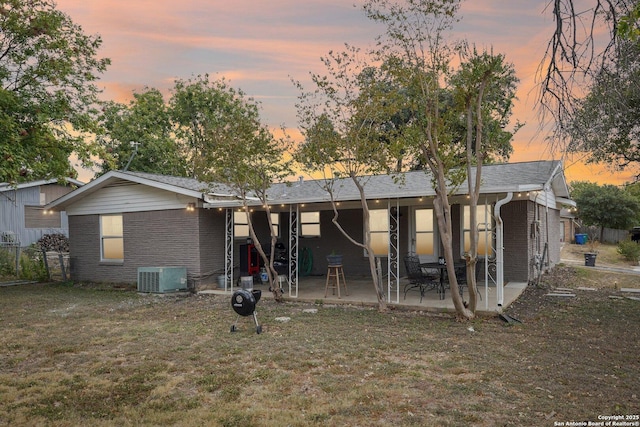 back house at dusk featuring cooling unit, a patio area, and a yard