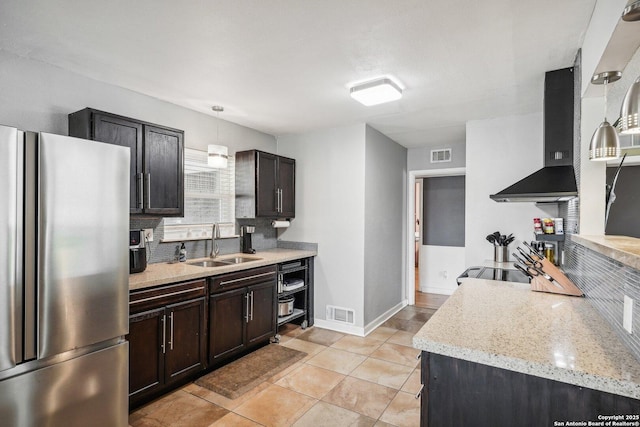 kitchen featuring stainless steel fridge, light stone counters, wall chimney exhaust hood, sink, and hanging light fixtures