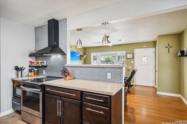 kitchen featuring tasteful backsplash, wall chimney exhaust hood, dark brown cabinetry, decorative light fixtures, and stainless steel electric range oven