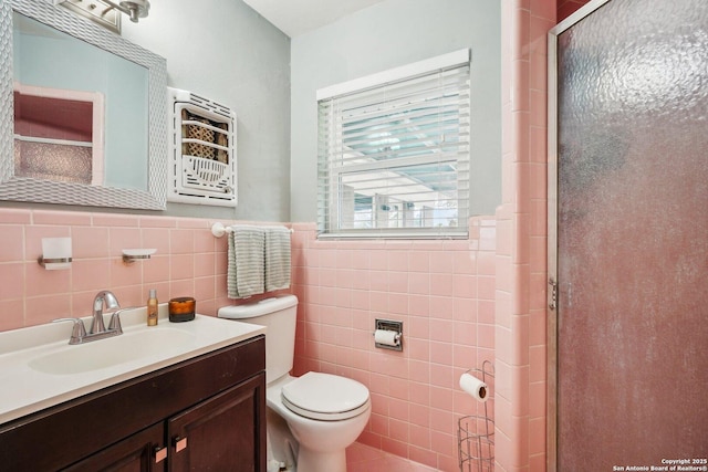 bathroom featuring vanity, toilet, a shower with shower door, and tile walls