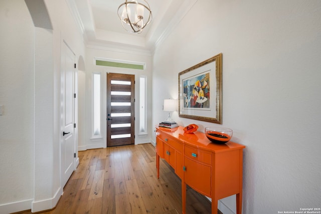 entrance foyer with arched walkways, crown molding, a raised ceiling, light wood-style floors, and a chandelier