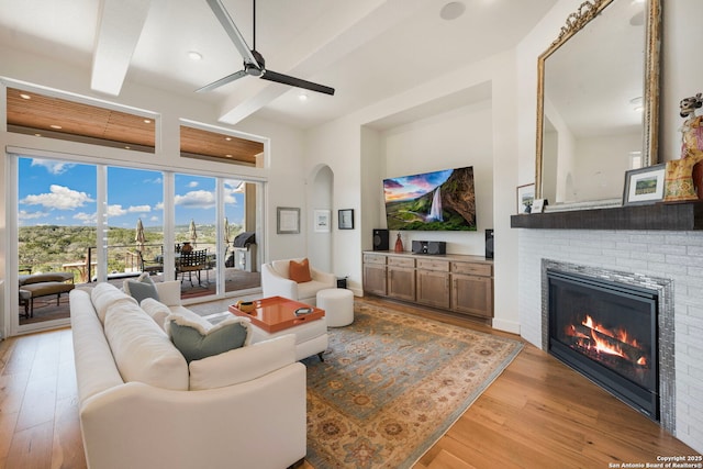 living area with light wood-type flooring, a fireplace, arched walkways, and beamed ceiling