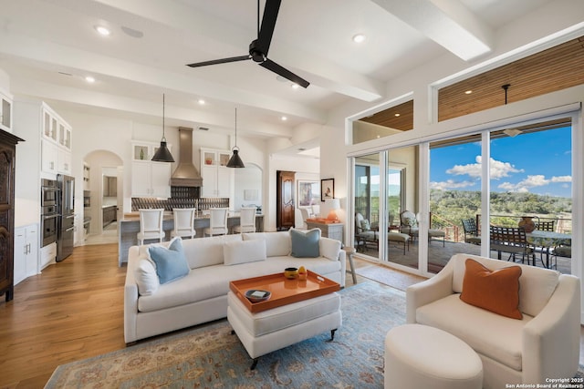 living area with arched walkways, a ceiling fan, beamed ceiling, wood finished floors, and recessed lighting