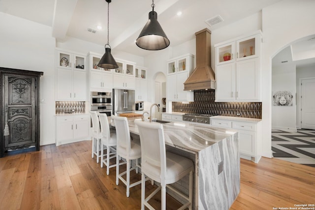 kitchen featuring visible vents, arched walkways, custom exhaust hood, stainless steel appliances, and a sink