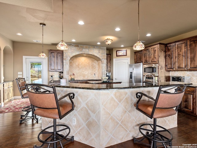 kitchen featuring a center island with sink, a kitchen breakfast bar, hanging light fixtures, appliances with stainless steel finishes, and tasteful backsplash