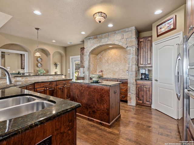 kitchen with sink, a center island, dark wood-type flooring, backsplash, and pendant lighting