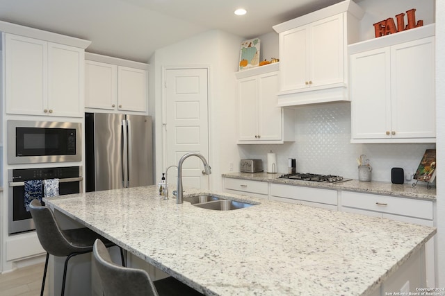 kitchen with a center island with sink, sink, light stone countertops, appliances with stainless steel finishes, and white cabinetry