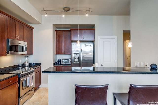 kitchen featuring light tile patterned flooring, a kitchen bar, appliances with stainless steel finishes, kitchen peninsula, and pendant lighting