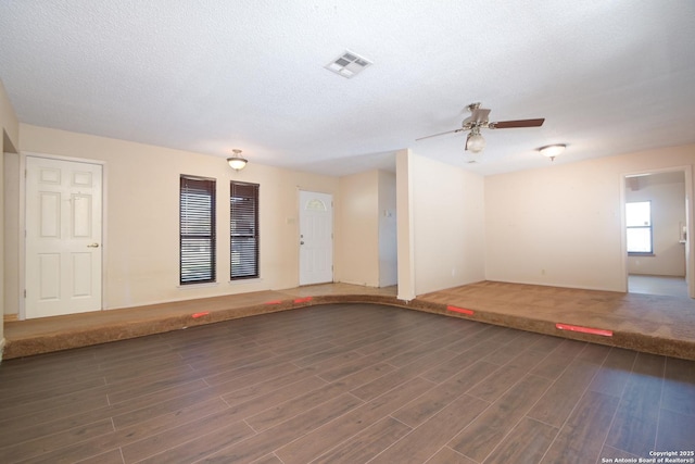 unfurnished room with a textured ceiling, ceiling fan, and dark wood-type flooring