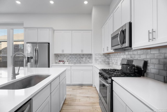 kitchen with backsplash, stainless steel appliances, sink, light hardwood / wood-style flooring, and white cabinets