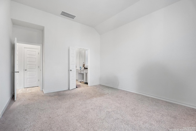 unfurnished bedroom with ensuite bath, light colored carpet, and vaulted ceiling