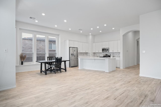 kitchen featuring a kitchen island with sink, decorative backsplash, appliances with stainless steel finishes, light hardwood / wood-style floors, and white cabinetry