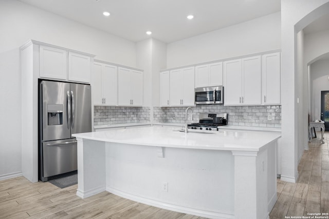 kitchen featuring white cabinets, light wood-type flooring, a kitchen island with sink, and appliances with stainless steel finishes