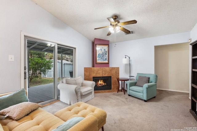 living area with light carpet, a textured ceiling, vaulted ceiling, ceiling fan, and a tile fireplace