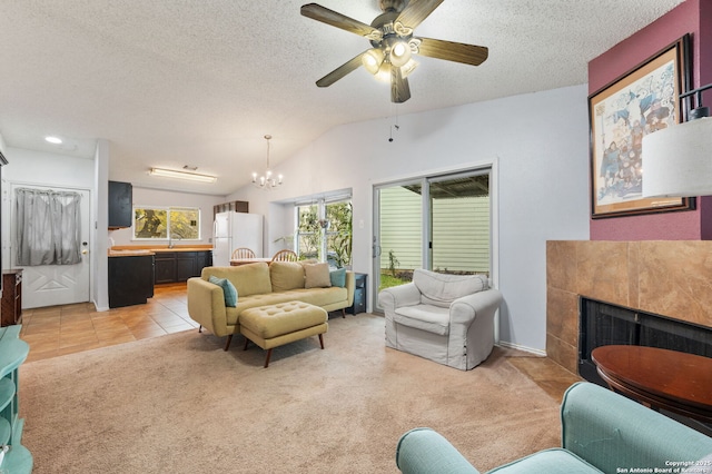 carpeted living room with ceiling fan with notable chandelier, lofted ceiling, a textured ceiling, and a tile fireplace