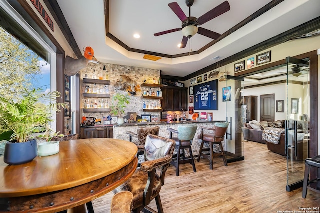 bar featuring dark brown cabinetry, ceiling fan, light hardwood / wood-style flooring, crown molding, and a tray ceiling