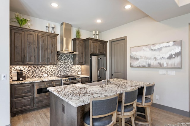 kitchen featuring sink, wall chimney exhaust hood, an island with sink, light hardwood / wood-style floors, and high end appliances