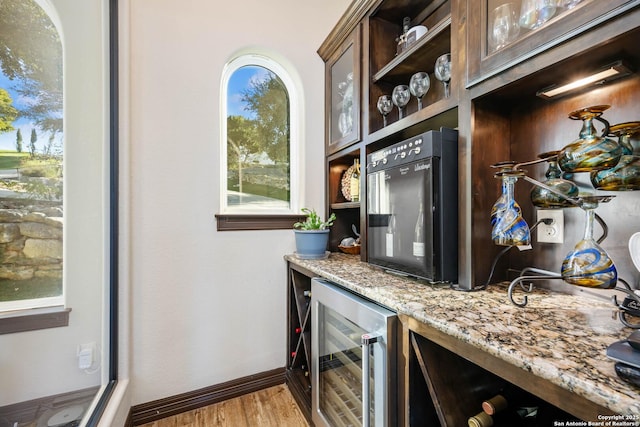 bar featuring light stone counters, light hardwood / wood-style flooring, and beverage cooler