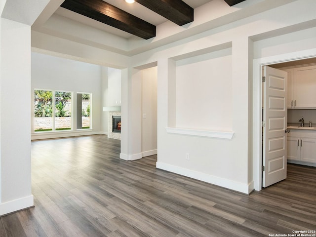 unfurnished living room featuring a towering ceiling, dark hardwood / wood-style flooring, sink, beam ceiling, and a stone fireplace