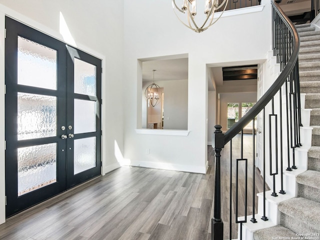 foyer featuring hardwood / wood-style flooring, french doors, a towering ceiling, and an inviting chandelier