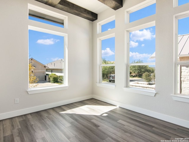 unfurnished room featuring beam ceiling, wood-type flooring, and a healthy amount of sunlight