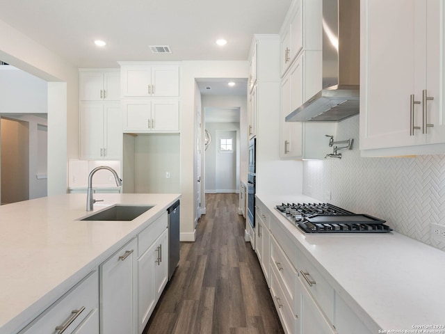 kitchen featuring sink, wall chimney range hood, backsplash, white cabinets, and appliances with stainless steel finishes