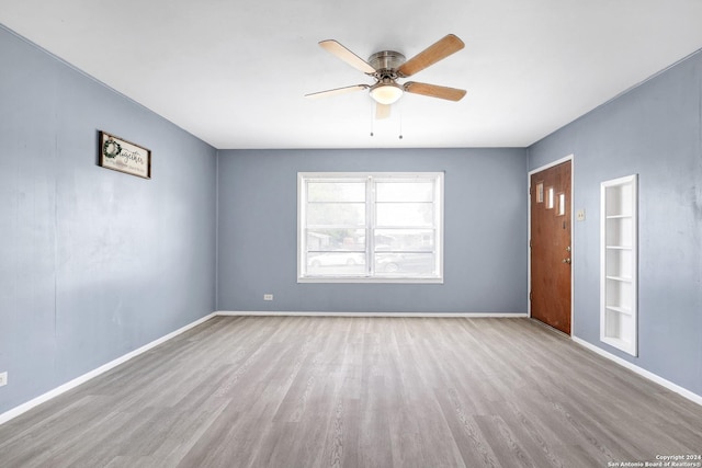 empty room with ceiling fan, built in features, and light wood-type flooring