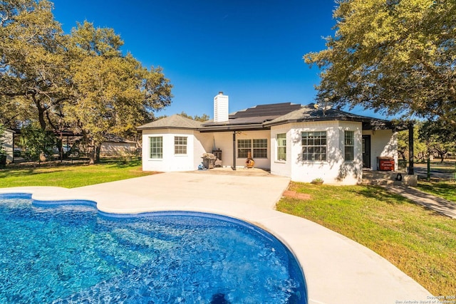 rear view of property featuring a lawn, a patio, and solar panels