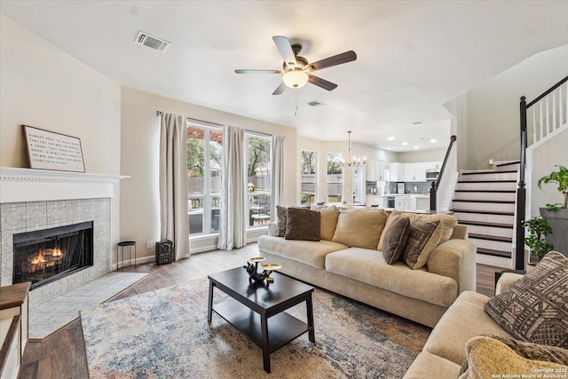 living room with light wood-type flooring, ceiling fan with notable chandelier, and a tiled fireplace