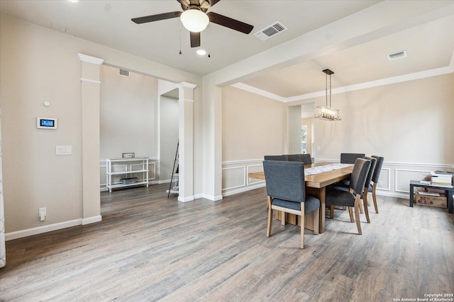 dining room with wood-type flooring, ceiling fan with notable chandelier, and ornate columns