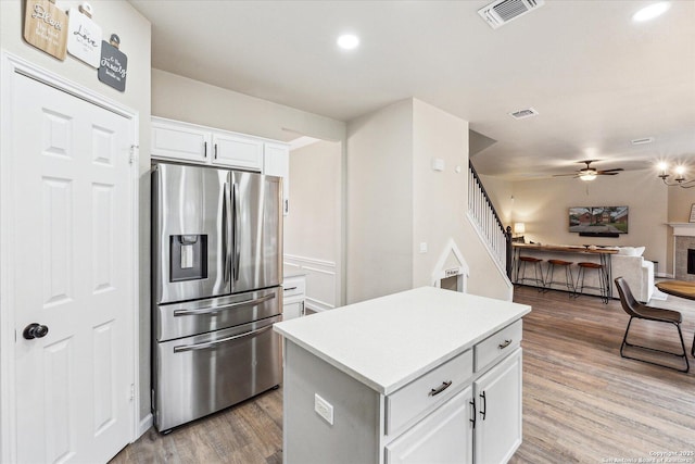 kitchen with stainless steel refrigerator with ice dispenser, a kitchen island, ceiling fan, light hardwood / wood-style flooring, and white cabinetry