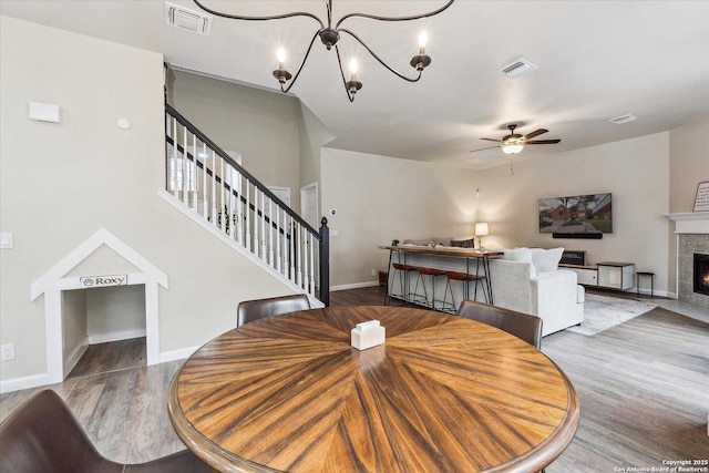 dining room featuring hardwood / wood-style floors, ceiling fan with notable chandelier, and a stone fireplace