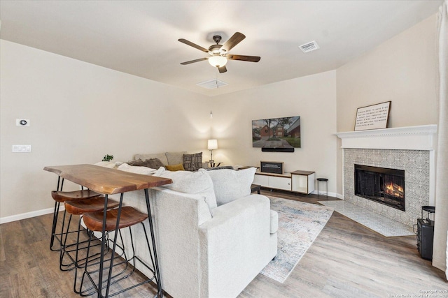 living room with a tile fireplace, ceiling fan, and wood-type flooring