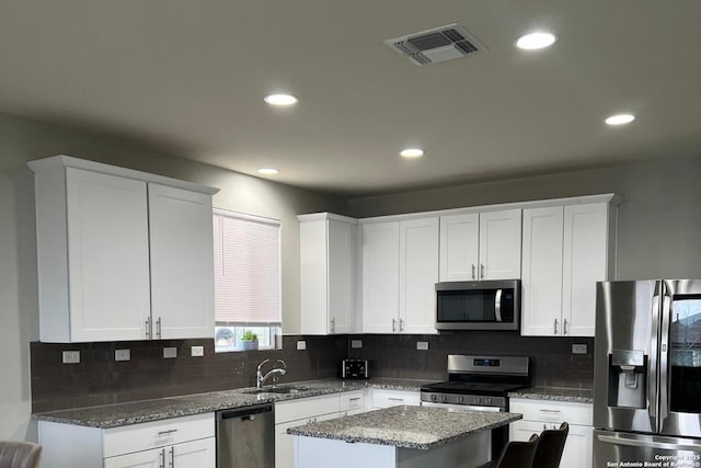 kitchen featuring appliances with stainless steel finishes, backsplash, white cabinetry, and a kitchen island