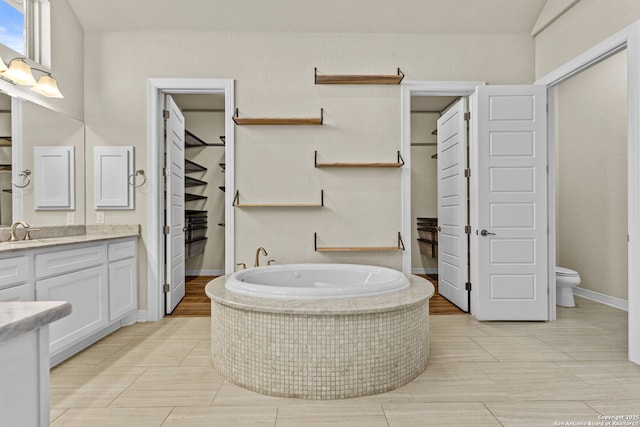 bathroom with vanity, a relaxing tiled tub, and toilet