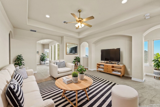 living room with a tray ceiling, ceiling fan, and light carpet